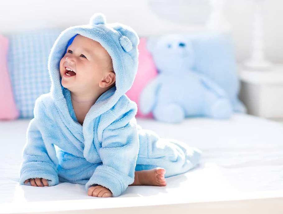 Smiling baby in a blue hooded robe sitting on a bed
